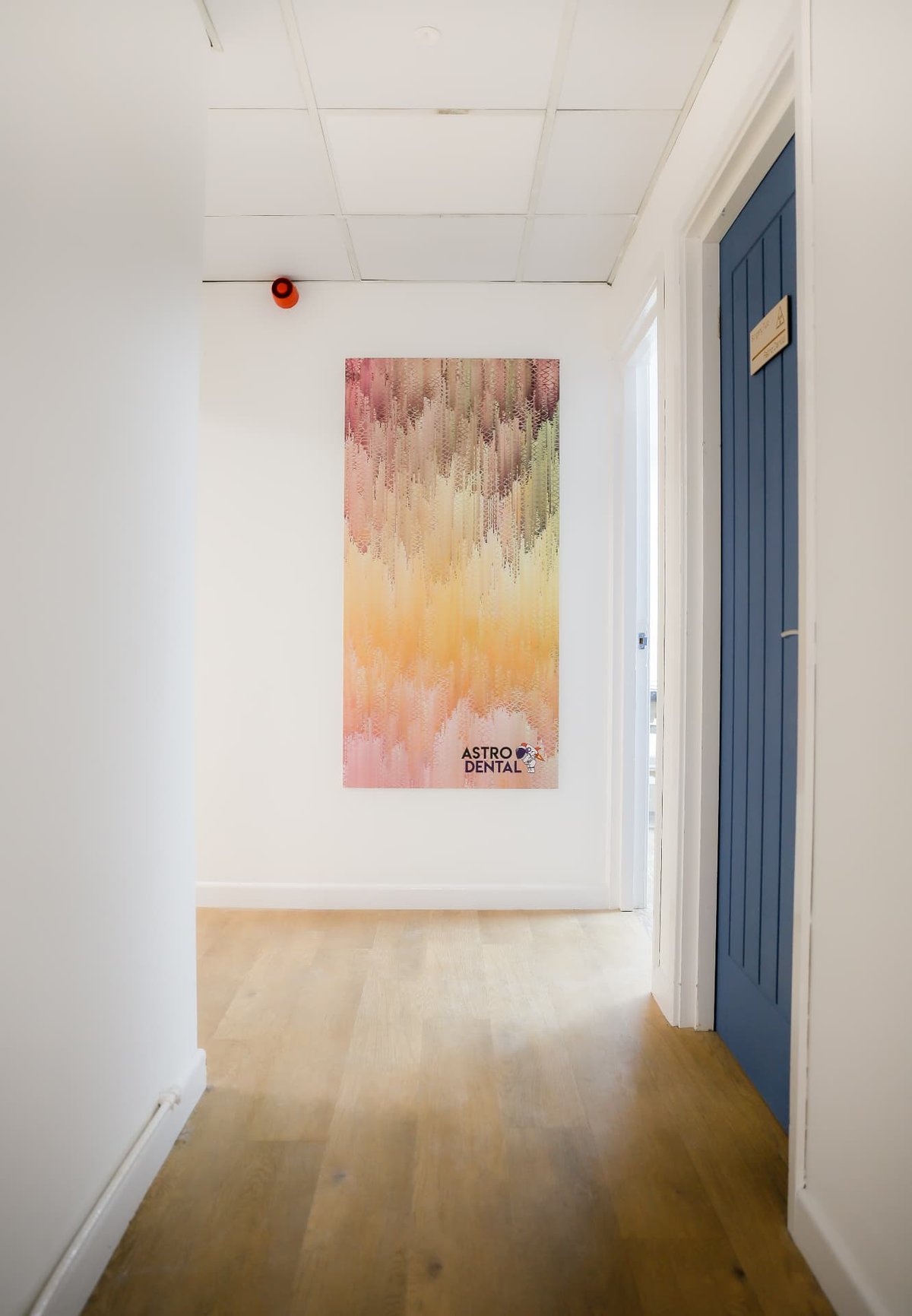 The corridor at Astro Dental leading to the surgeries, with a tall pastel canvas on the end wall